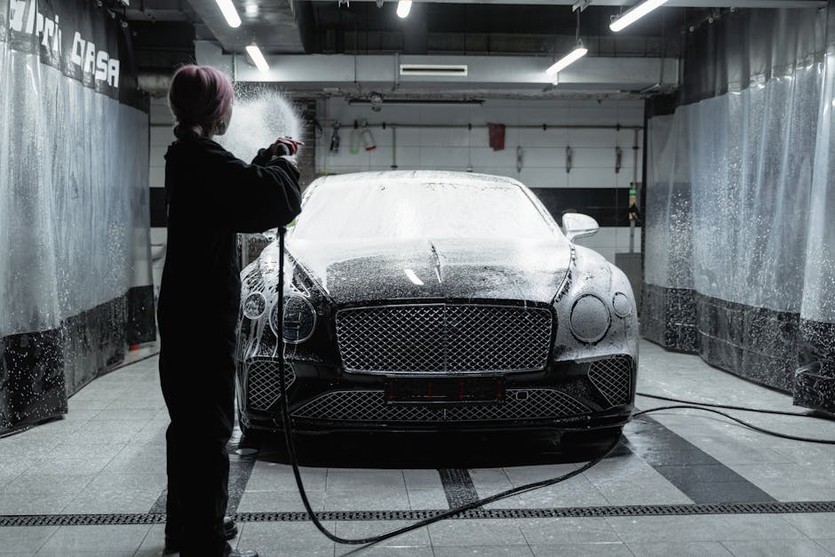 A black Bentley being washed with soap at an indoor car wash facility by a woman in a black sweater.